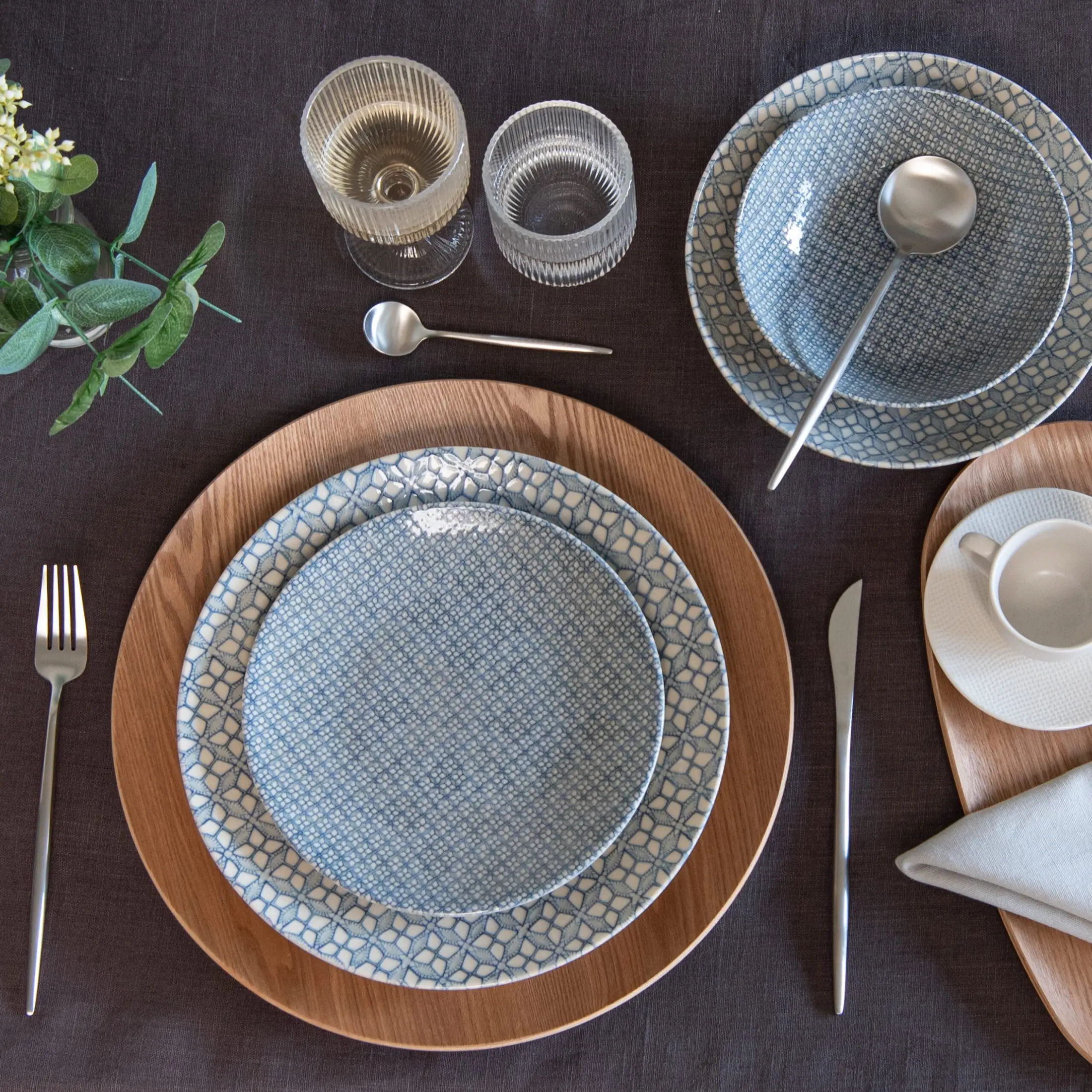 Mesa puesta con plato estampado azul sobre bajoplato de madera y copas